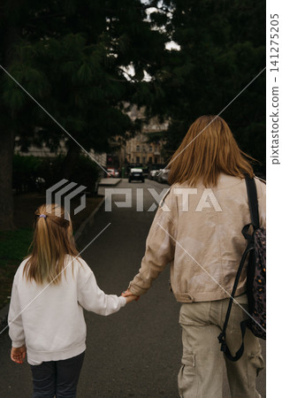 Mom holds hands with little daughter while walking on a city street in the afternoon Mom holds hands with little daughter while walking on a city street in the afternoon 141275205