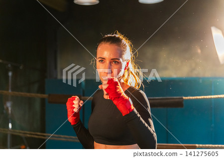 Women self defense girl power. Strong woman fighter punching with red boxing wraps sports protective bandages. Girl punching training punches looking concentrated straight. Fit body workout Women self defense girl power. Strong woman fighter punching with red boxing wraps sports protective bandages. Girl punching training punches looking concentrated straight. Fit body workout 141275605