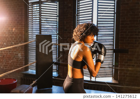Outcry independent girl power. Angry African American woman fighter with boxing gloves looking serious aggressive standing on boxing ring. Strong powerful fighter girl training punches Outcry independent girl power. Angry African American woman fighter with boxing gloves looking serious aggressive standing on boxing ring. Strong powerful fighter girl training punches 141275612