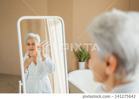 Love yourself. Beautiful old woman enjoying mirror reflection. Senior older lady spending morning in bathroom looking at mirror confident happy. Woman doing daily morning beauty routine. Self love Love yourself. Beautiful old woman enjoying mirror reflection. Senior older lady spending morning in bathroom looking at mirror confident happy. Woman doing daily morning beauty routine. Self love 141275642