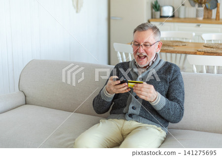 Senior man shopping online holding smartphone paying with credit card. Old grandfather buying on Internet enter credit card details. Online shopping delivery service Older generation modern tech usage Senior man shopping online holding smartphone paying with credit card. Old grandfather buying on Internet enter credit card details. Online shopping delivery service Older generation modern tech usage 141275695