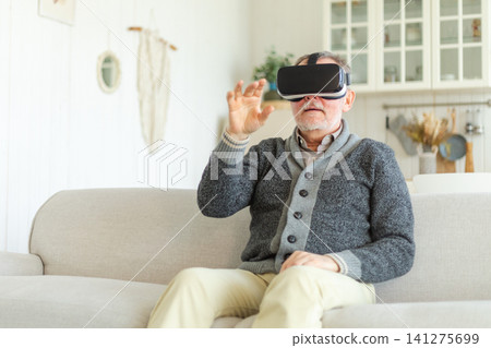 Excited mature senior man wearing using virtual reality metaverse VR glasses headset at home. Grandfather touching air during VR experience on virtual reality helmet. Simulation hi-tech videogame Excited mature senior man wearing using virtual reality metaverse VR glasses headset at home. Grandfather touching air during VR experience on virtual reality helmet. Simulation hi-tech videogame 141275699