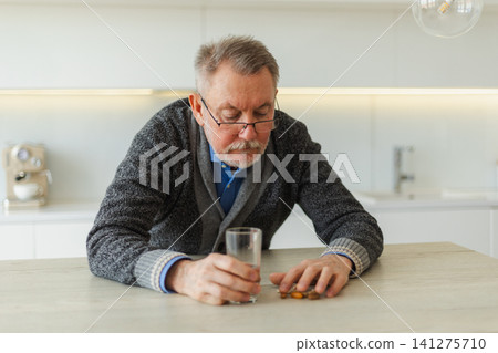 Middle aged senior man holding medical pill and glass of water. Mature old senior grandfather taking medication cure pills vitamin. Age prescription medicine healthcare therapy concept Middle aged senior man holding medical pill and glass of water. Mature old senior grandfather taking medication cure pills vitamin. Age prescription medicine healthcare therapy concept 141275710