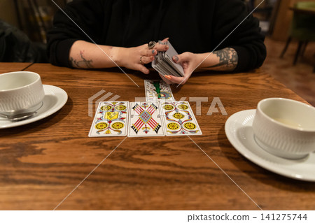 Tarot cards and fortune telling. Soothsayer predicting future with tarot cards. Unrecognizable mysterious fortuneteller holding tarot cards forecasting future for client. Future reading esoteric Tarot cards and fortune telling. Soothsayer predicting future with tarot cards. Unrecognizable mysterious fortuneteller holding tarot cards forecasting future for client. Future reading esoteric 141275744