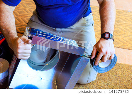 Worker installs ductwork using tape in construction setting Worker installs ductwork using tape in construction setting 141275785