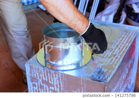 Worker installs duct piece on metal box in workshop during home improvement Worker installs duct piece on metal box in workshop during home improvement 141275786
