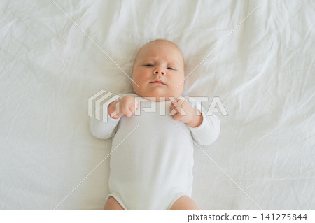 Happy baby. Cute little newborn girl with smiling face lying on bed in bedroom. Infant baby resting playing lying down on white blanket at home. Motherhood happy child childcare concept Happy baby. Cute little newborn girl with smiling face lying on bed in bedroom. Infant baby resting playing lying down on white blanket at home. Motherhood happy child childcare concept 141275844