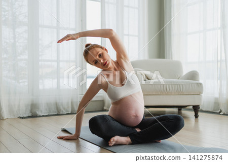 Pregnancy yoga fitness workout training. Pregnant woman practicing yoga at home. Pregnant girl doing sports exercise on yoga mat indoor. Woman with big belly have fitness training practicing asana Pregnancy yoga fitness workout training. Pregnant woman practicing yoga at home. Pregnant girl doing sports exercise on yoga mat indoor. Woman with big belly have fitness training practicing asana 141275874