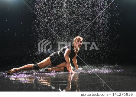 Contemporary woman dancer posing in rain water on black background. Female artist performer dancing with expression. Modern ballerina dancing in darkness. Passion dance in dark. Flexibility balance Contemporary woman dancer posing in rain water on black background. Female artist performer dancing with expression. Modern ballerina dancing in darkness. Passion dance in dark. Flexibility balance 141275939
