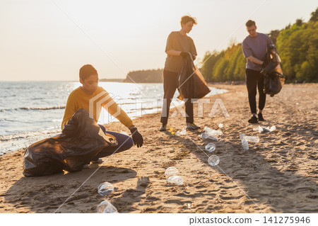 Earth day. Volunteers activists team collects garbage cleaning of beach coastal zone. Woman mans puts plastic trash in garbage bag on ocean shore. Environmental conservation coastal zone cleaning Earth day. Volunteers activists team collects garbage cleaning of beach coastal zone. Woman mans puts plastic trash in garbage bag on ocean shore. Environmental conservation coastal zone cleaning 141275946