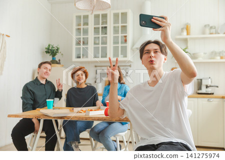 Cheers Funky mood. Happy group of friends make selfie. Man taking photo of friends at party. Group of multiracial young people taking photo on phone. Young people enjoy their company smile have fun Cheers Funky mood. Happy group of friends make selfie. Man taking photo of friends at party. Group of multiracial young people taking photo on phone. Young people enjoy their company smile have fun 141275974