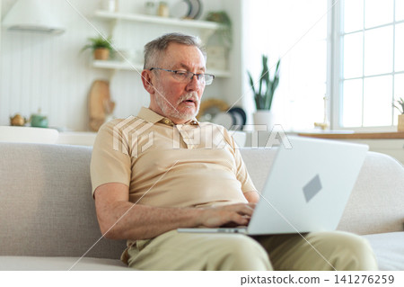 Confident stylish happy middle aged senior man using laptop at home. Stylish older mature 60s beard grandfather sitting at couch looking at computer screen typing chatting reading writing email Confident stylish happy middle aged senior man using laptop at home. Stylish older mature 60s beard grandfather sitting at couch looking at computer screen typing chatting reading writing email 141276259