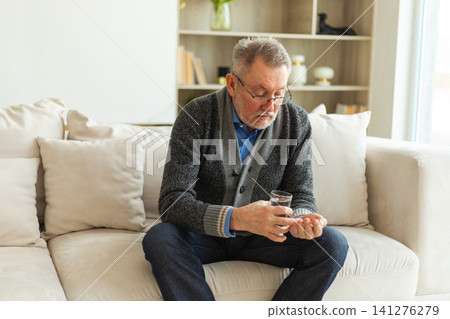 Middle aged senior man holding medical pill and glass of water. Mature old senior grandfather taking medication cure pills vitamin. Age prescription medicine healthcare therapy concept Middle aged senior man holding medical pill and glass of water. Mature old senior grandfather taking medication cure pills vitamin. Age prescription medicine healthcare therapy concept 141276279