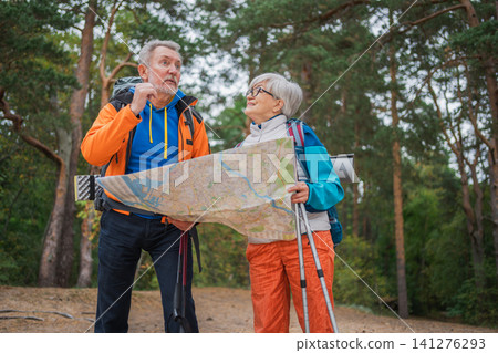 Hiking tourism. Senior couple man woman looking track in paper map enjoying hiking in forest. Happy old people backpackers hikers enjoy walking hike trekking tourism active vacation beauty of nature Hiking tourism. Senior couple man woman looking track in paper map enjoying hiking in forest. Happy old people backpackers hikers enjoy walking hike trekking tourism active vacation beauty of nature 141276293