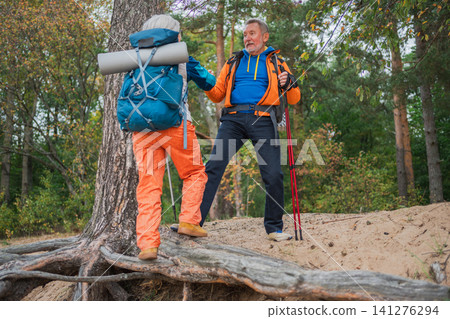 Hiking adventure. Man helping hand woman on hiking in forest. Senior couple enjoying outdoor recreation hiking. Happy old people backpackers hikers enjoy walking hike trekking tourism active vacation Hiking adventure. Man helping hand woman on hiking in forest. Senior couple enjoying outdoor recreation hiking. Happy old people backpackers hikers enjoy walking hike trekking tourism active vacation 141276294