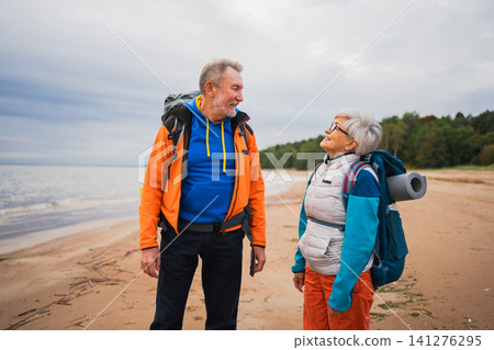Hiking tourism adventure. Senior couple man woman enjoying outdoor recreation hiking on beach. Happy old people backpackers hikers enjoy walking hike trekking tourism active vacation beauty of nature Hiking tourism adventure. Senior couple man woman enjoying outdoor recreation hiking on beach. Happy old people backpackers hikers enjoy walking hike trekking tourism active vacation beauty of nature 141276295