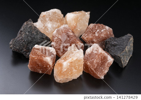 Natural crystals of pink and black rock salt lined up against a black background. Natural crystals of pink and black rock salt lined up against a black background. 141278429