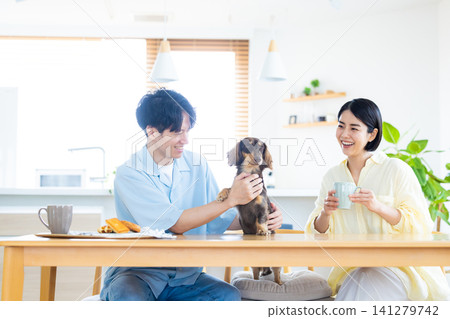與狗狗共度的家庭生活:一對夫婦在客廳和心愛的狗狗一起玩耍。 與狗狗共度的家庭生活:一對夫婦在客廳和心愛的狗狗一起玩耍。 141279742