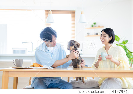 與狗狗共度的家庭生活:一對夫婦在客廳和心愛的狗狗一起玩耍。 與狗狗共度的家庭生活:一對夫婦在客廳和心愛的狗狗一起玩耍。 141279743