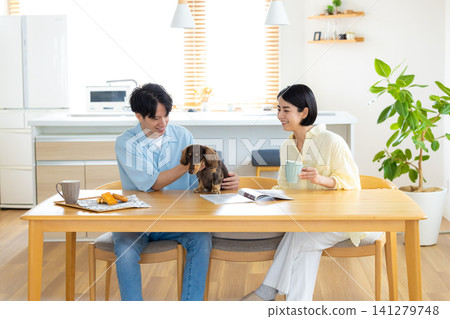 與狗狗共度的家庭生活:一對夫婦在客廳和心愛的狗狗一起玩耍。 與狗狗共度的家庭生活:一對夫婦在客廳和心愛的狗狗一起玩耍。 141279748