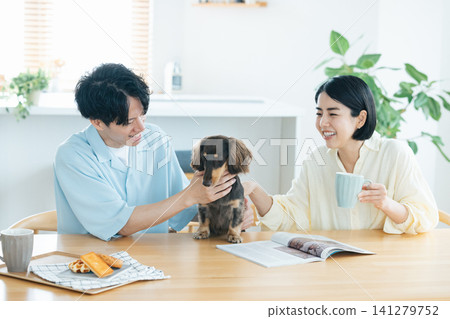 與狗狗共度的家庭生活:一對夫婦在客廳和心愛的狗狗一起玩耍。 與狗狗共度的家庭生活:一對夫婦在客廳和心愛的狗狗一起玩耍。 141279752