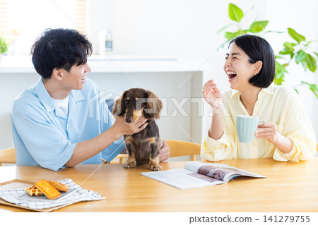 與狗狗共度的家庭生活:一對夫婦在客廳和心愛的狗狗一起玩耍。 與狗狗共度的家庭生活:一對夫婦在客廳和心愛的狗狗一起玩耍。 141279755