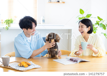 與狗狗共度的家庭生活:一對夫婦在客廳和心愛的狗狗一起玩耍。 與狗狗共度的家庭生活:一對夫婦在客廳和心愛的狗狗一起玩耍。 141279757