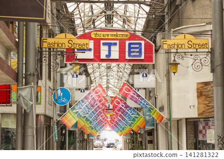 The entrance to a retro Showa-era shopping street, adorned with colorful flags and a "Fashion Street" sign. 141281322