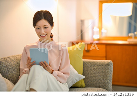 A woman in her 40s relaxing in her room at night and watching her tablet. 141281339