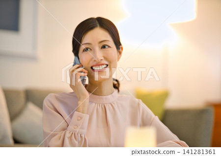 一位四十多歲的女性晚上在房間裡放鬆,看著她的智慧型手機。 一位四十多歲的女性晚上在房間裡放鬆,看著她的智慧型手機。 141281361