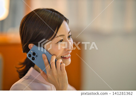 一位四十多歲的女性晚上在房間裡放鬆,看著她的智慧型手機。 一位四十多歲的女性晚上在房間裡放鬆,看著她的智慧型手機。 141281362