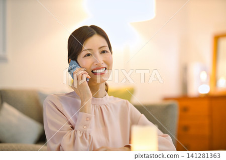 A woman in her 40s relaxing in her room at night and looking at her smartphone. A woman in her 40s relaxing in her room at night and looking at her smartphone. 141281363