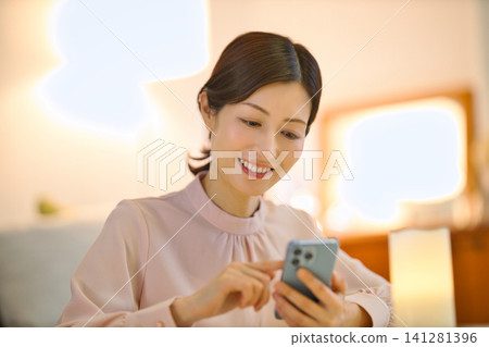 一位四十多歲的女性晚上在房間裡放鬆,看著她的智慧型手機。 一位四十多歲的女性晚上在房間裡放鬆,看著她的智慧型手機。 141281396