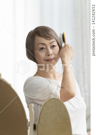 A senior woman styling her hair with a brush. A senior woman styling her hair with a brush. 141282652