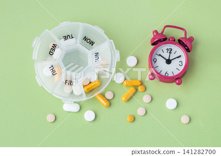 Pill box organizer with medication and alarm clock on green background Pill box organizer with medication and alarm clock on green background 141282700