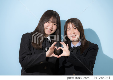 兩位面帶微笑的日本高中女生手牽手組成心形；這是友誼和青春的象徵，她們微笑著直視鏡頭。 141283081
