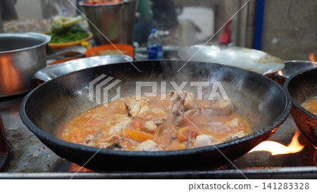 Close-up of chicken karahi in a wok over flames, steam rising, with cooking equipment around, street food Close-up of chicken karahi in a wok over flames, steam rising, with cooking equipment around, street food 141283328