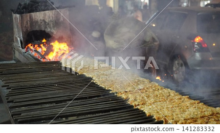 Meat kebabs grilling over hot coals on a large grill, smoke rising, street food 141283332