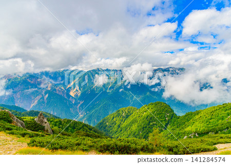 A summer afternoon view of the Northern Alps mountain range towards Ura-Ginza, seen through the clouds from near Enzanso mountain hut on Mount Tsubakuro. A summer afternoon view of the Northern Alps mountain range towards Ura-Ginza, seen through the clouds from near Enzanso mountain hut on Mount Tsubakuro. 141284574