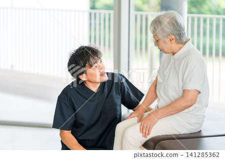 男性物理治療師和整骨師傾聽老年女性關於膝蓋疼痛的訴求。 男性物理治療師和整骨師傾聽老年女性關於膝蓋疼痛的訴求。 141285362