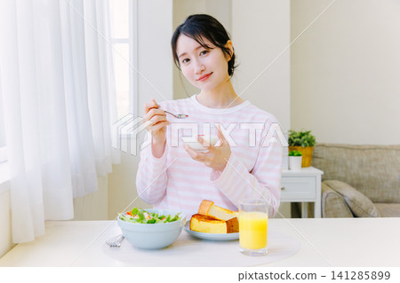 A young woman eating yogurt for breakfast A young woman eating yogurt for breakfast 141285899