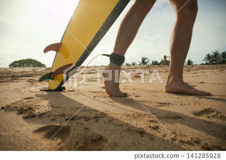 Surfer walks on sandy beach with surfboard ready for action Surfer walks on sandy beach with surfboard ready for action 141285928