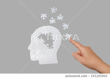 A hand positions a puzzle piece into a human head silhouette design A hand positions a puzzle piece into a human head silhouette design 141285942