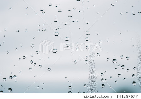 raindrops during raining in the rainy day outside window glass with a blurred background with water droplets flowing down the surface raindrops during raining in the rainy day outside window glass with a blurred background with water droplets flowing down the surface 141287677
