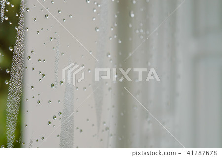 raindrops during raining in the rainy day outside window glass with a blurred background with water droplets flowing down the surface raindrops during raining in the rainy day outside window glass with a blurred background with water droplets flowing down the surface 141287678
