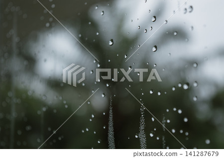 raindrops during raining in the rainy day outside window glass with a blurred background with water droplets flowing down the surface raindrops during raining in the rainy day outside window glass with a blurred background with water droplets flowing down the surface 141287679