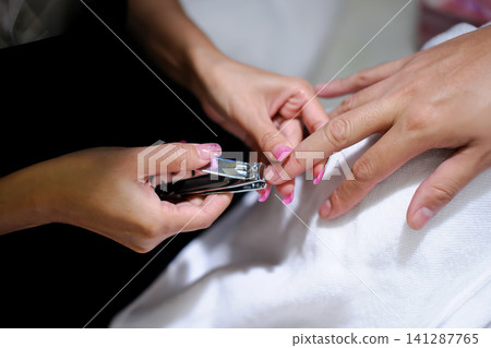 an employee of nail salon cutting customer nails in service. an employee of nail salon cutting customer nails in service. 141287765