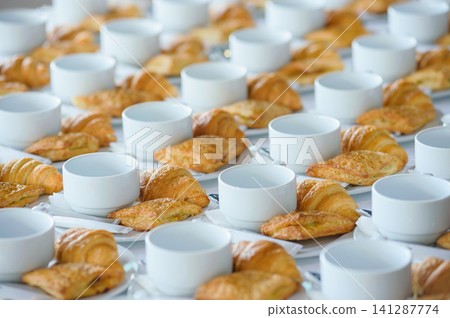 many line of croissant on a dish with empty coffee cups on the table ready to served for tea break in business conference many line of croissant on a dish with empty coffee cups on the table ready to served for tea break in business conference 141287774