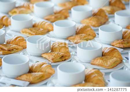 many line of croissant on a dish with empty coffee cups on the table ready to served for tea break in business conference many line of croissant on a dish with empty coffee cups on the table ready to served for tea break in business conference 141287775