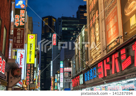 The evening in Nishi-Shinjuku, Tokyo. Giant neon signs and skyscrapers glow in the blue hour, creating a vibrant cityscape. 141287894
